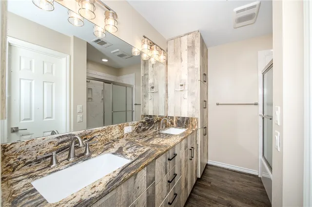 a bathroom with a granite countertop double vanity sink a mirror and a shower