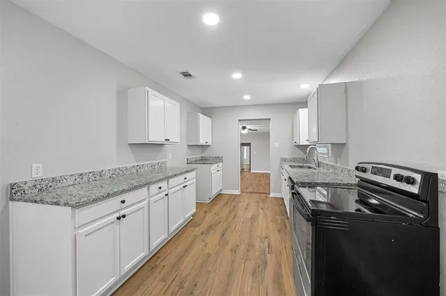 a kitchen with stainless steel appliances granite countertop a stove top oven a sink dishwasher and a refrigerator with wooden floor