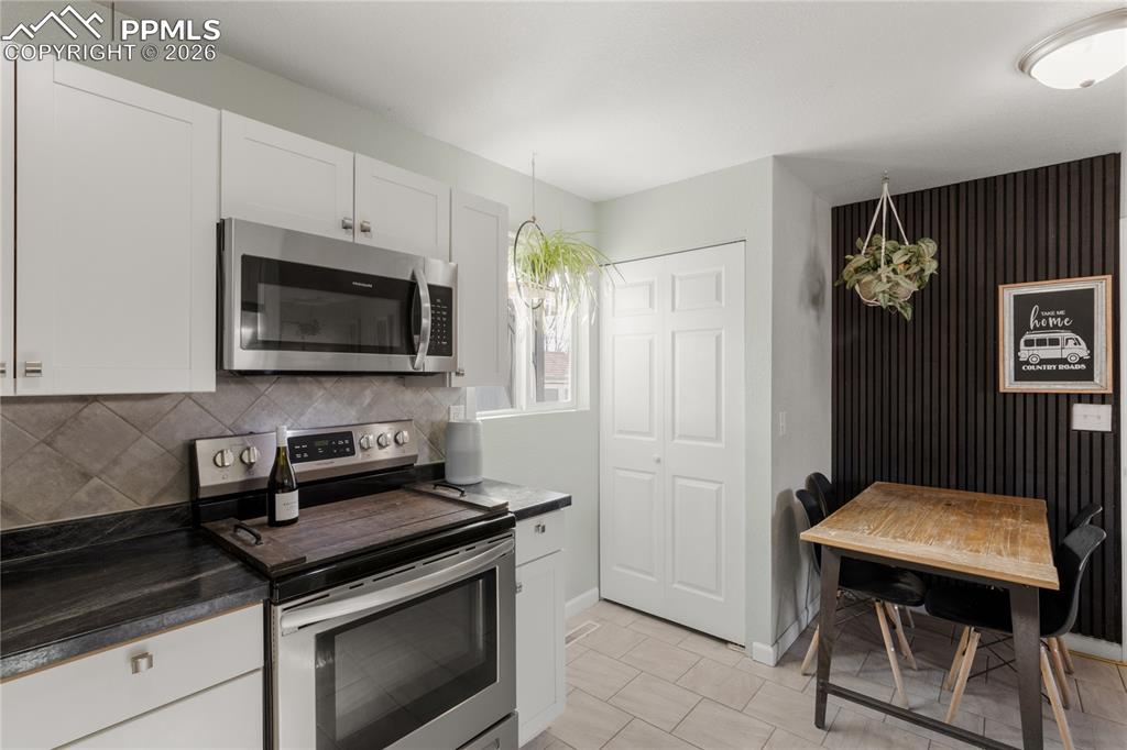 1703 Harrow Road Colorado Springs, CO 80906 - Photo 12 of 32 Kitchen featuring appliances with stainless steel finishes, dark countertops, white cabinets, decorative light fixtures, and decorative backsplash