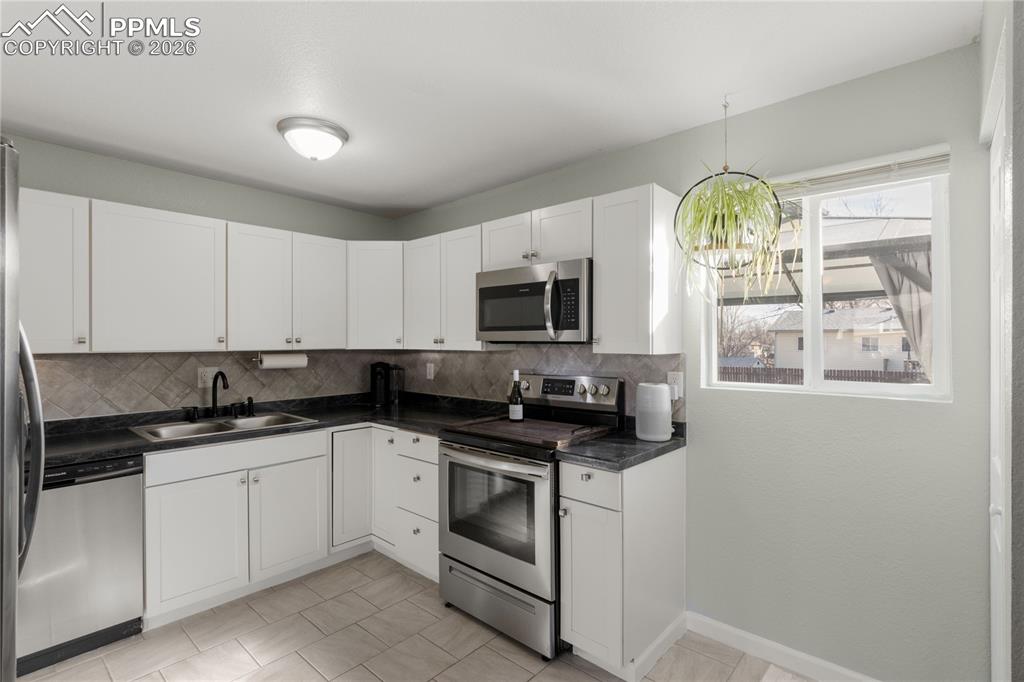 1703 Harrow Road Colorado Springs, CO 80906 - Photo 14 of 32 Kitchen with appliances with stainless steel finishes, white cabinetry, dark countertops, decorative light fixtures, and backsplash