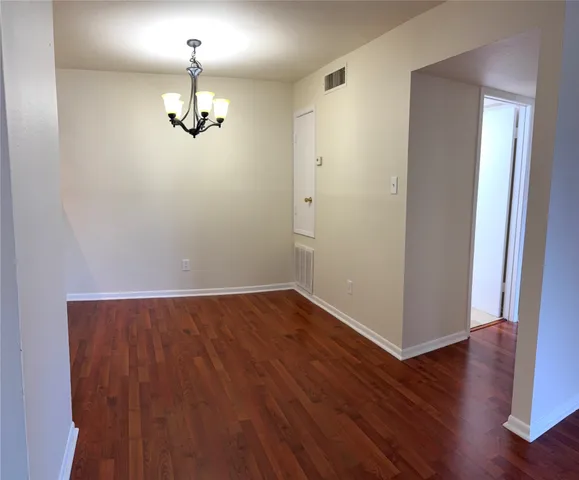 an empty room with wooden floor chandelier and windows