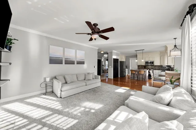 a living room with furniture kitchen area and a ceiling fan