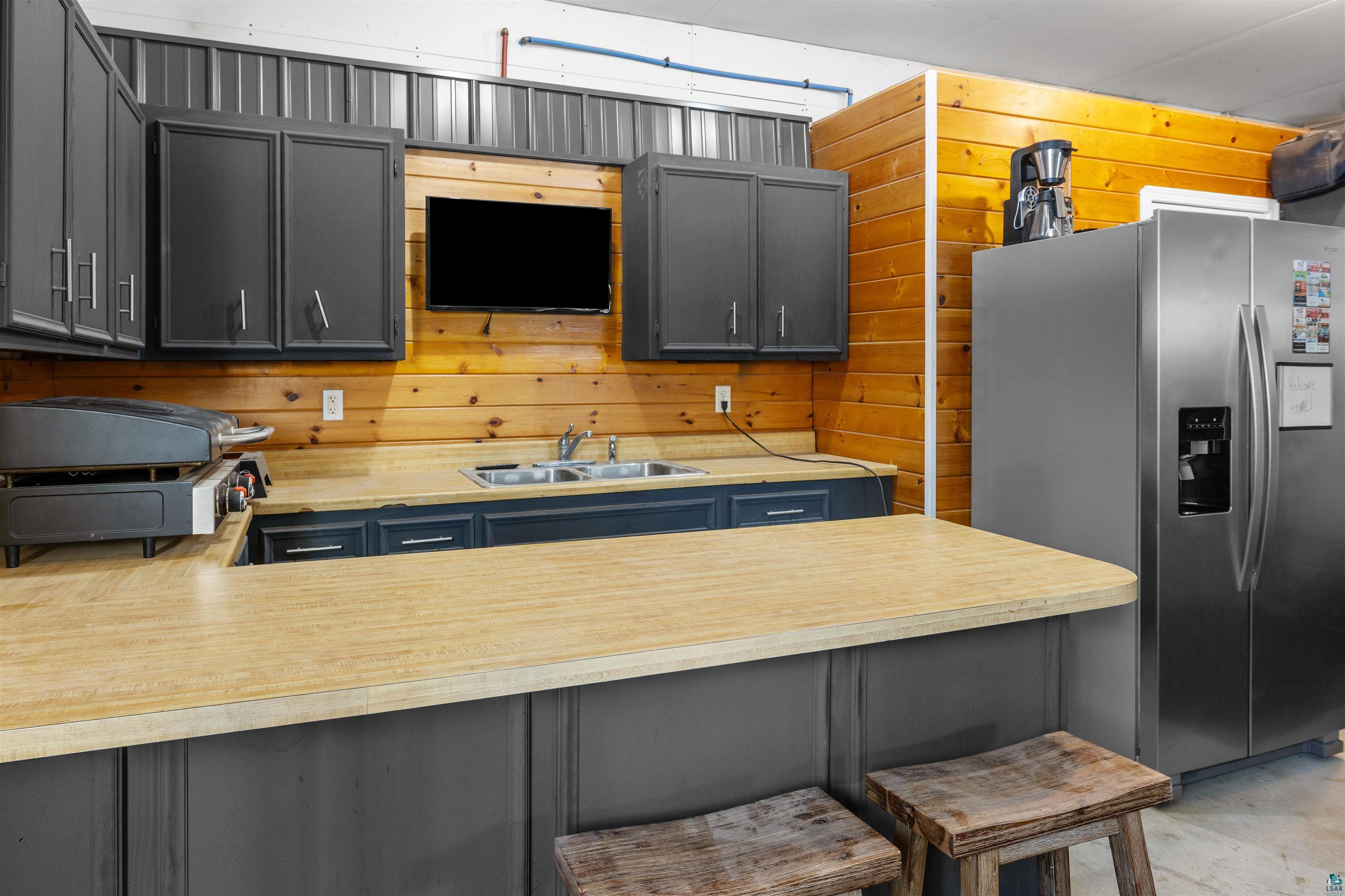 13462 Villa Road Ely, MN 55731 - Photo 25 of 68 Garage kitchen with gray cabinets, wood walls, light countertops, stainless steel fridge, and a peninsula