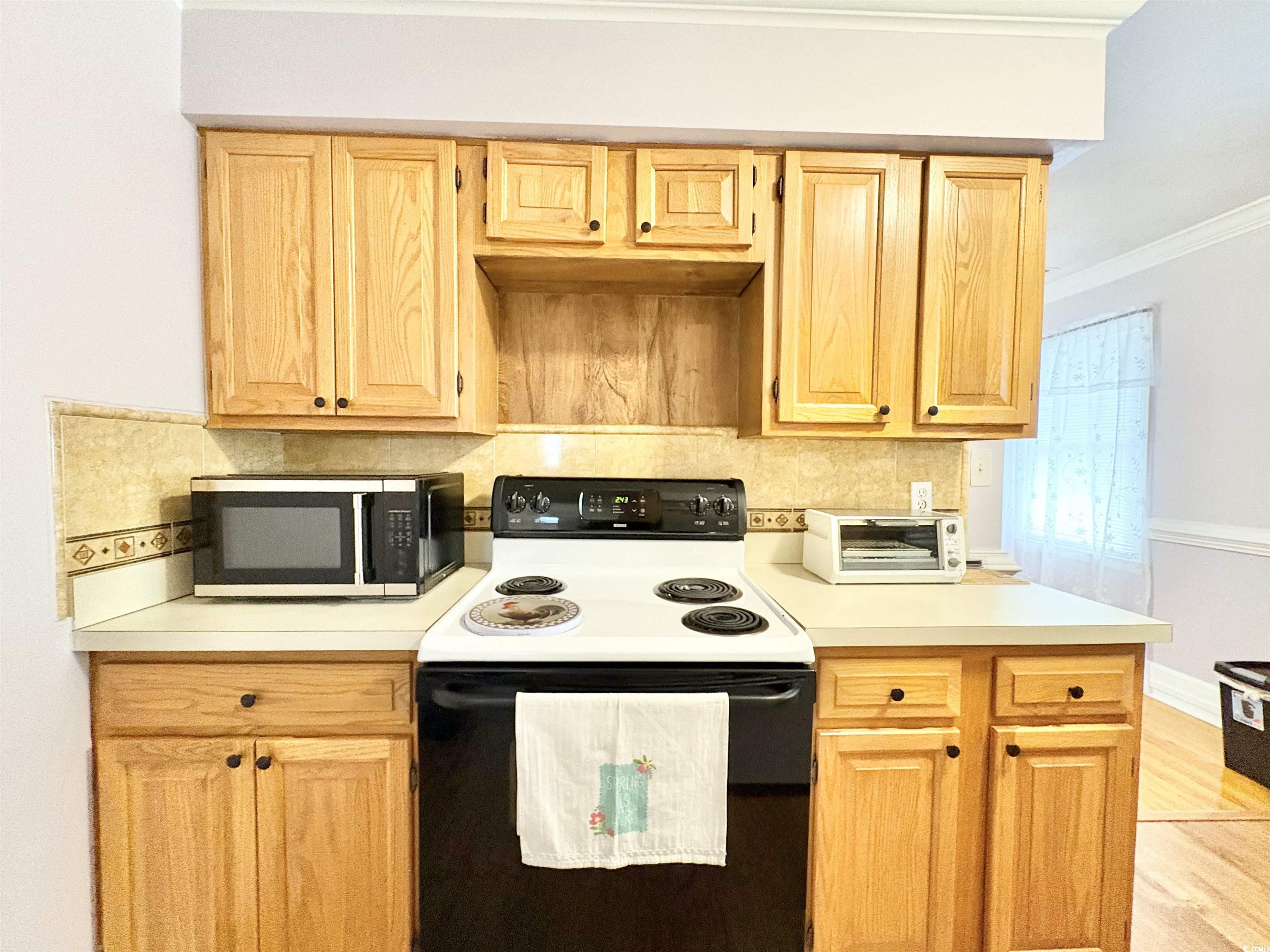 703 62nd Avenue North Myrtle Beach, SC 29577 - Photo 12 of 20 Kitchen with range with electric cooktop, light countertops, crown molding, wood finished floors, and tasteful backsplash