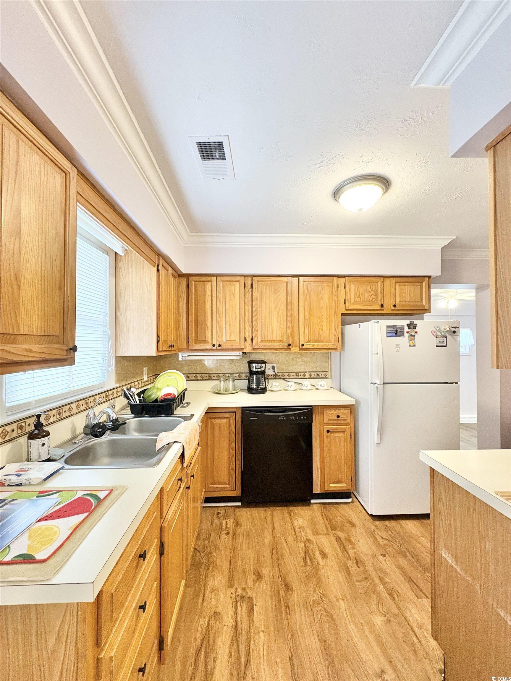 703 62nd Avenue North Myrtle Beach, SC 29577 - Photo 13 of 20 Kitchen featuring freestanding refrigerator, light countertops, crown molding, dishwasher, and light wood finished floors