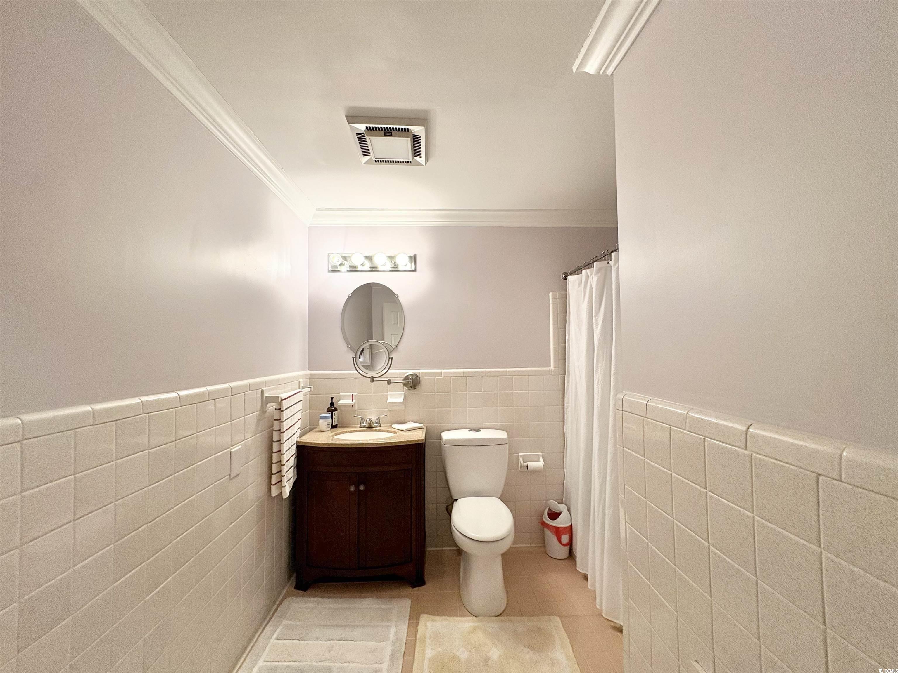 703 62nd Avenue North Myrtle Beach, SC 29577 - Photo 6 of 20 Full bath featuring a wainscoted wall, tile walls, a shower with curtain, vanity, and light tile patterned floors