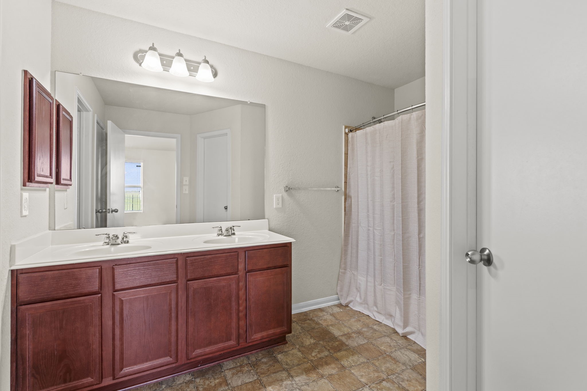 2110 Red Cedar Trail Rosenberg, TX 77471 - Photo 10 of 20 This full primary bathroom is designed for convenience, featuring an expansive wood-toned double vanity with dual integrated sinks and an oversized wall mirror. The functional layout includes a standard tub/shower combination, low-maintenance flooring, an integrated ceiling ventilation system.