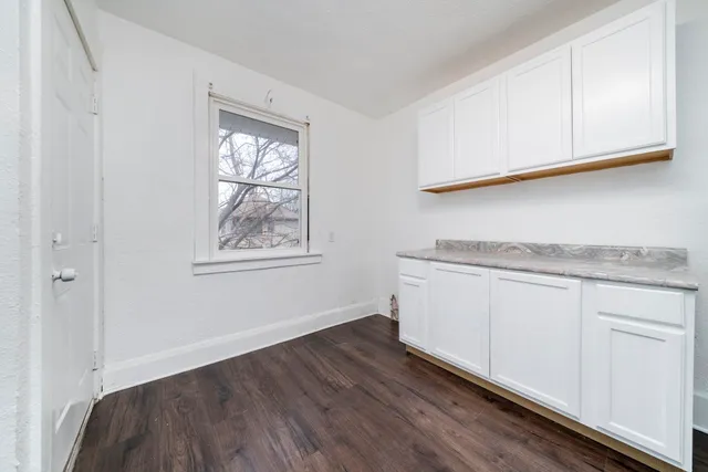 a utility room with granite countertop cabinets a window and a wooden floor