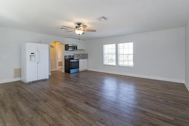 an empty room with wooden floor chandelier fan and windows