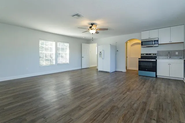 an empty room with wooden floor a ceiling fan and kitchen view
