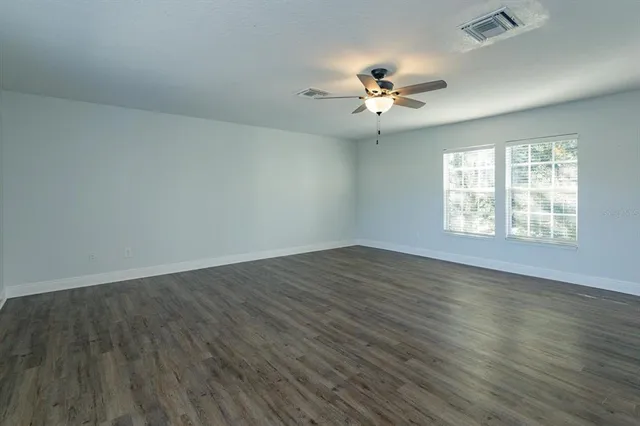 an empty room with wooden floor fan and windows