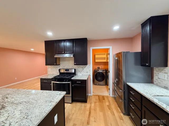 a kitchen with stainless steel appliances granite countertop sink stove refrigerator and wooden cabinets