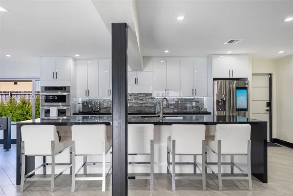 a kitchen with stainless steel appliances kitchen island granite countertop a table chairs refrigerator and microwave
