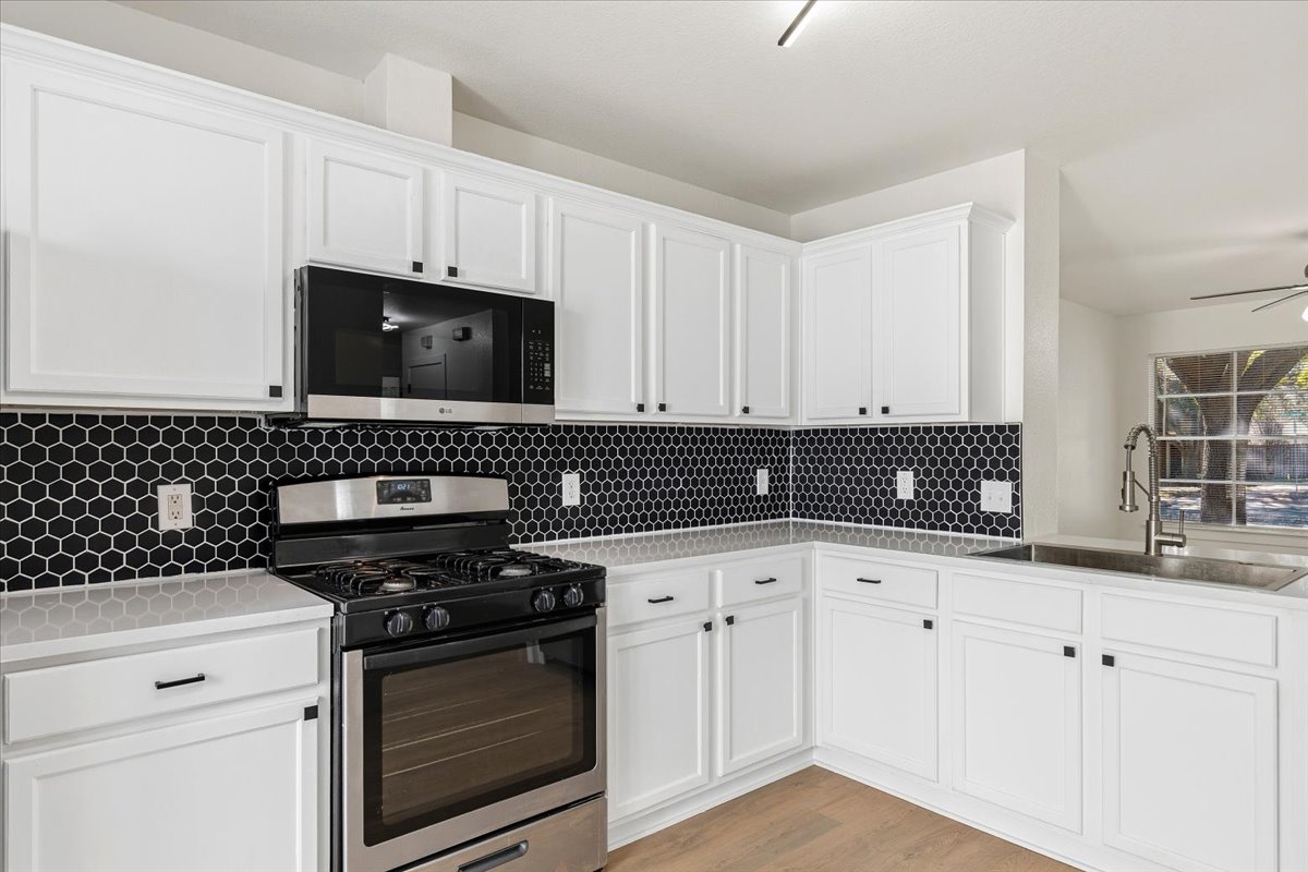 1007 Port Daniel Drive Leander, TX 78641 - Photo 8 of 21 Kitchen featuring stainless steel appliances, white cabinetry, backsplash, and light wood-style floors