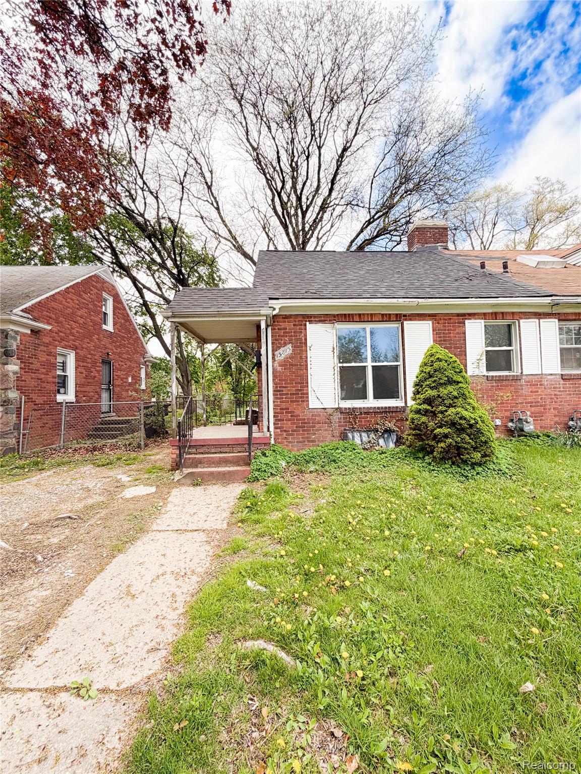 15815 Evergreen Road Detroit, MI 48223 - Photo 2 of 12 Brick exterior featuring white window shutters, a covered entry porch, a paved front walkway, and a sloped front lawn with green grass and foliage