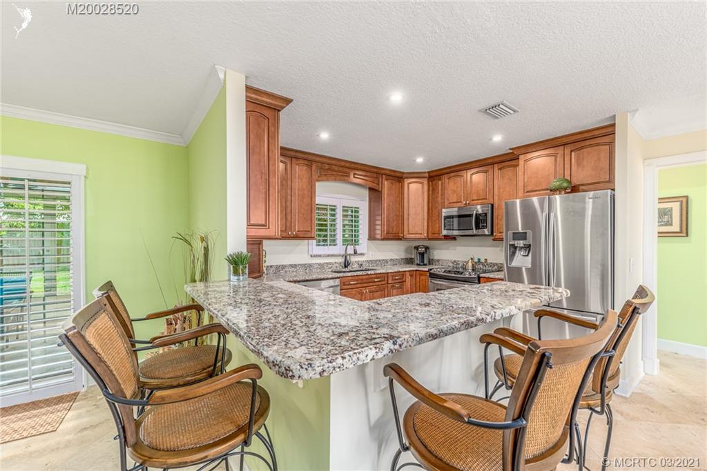 4780 Southeast Glen Ridge Trail Stuart, FL 34997 - Photo 16 of 31 a kitchen with granite countertop kitchen island stainless steel appliances a refrigerator a stove a dining table and chairs
