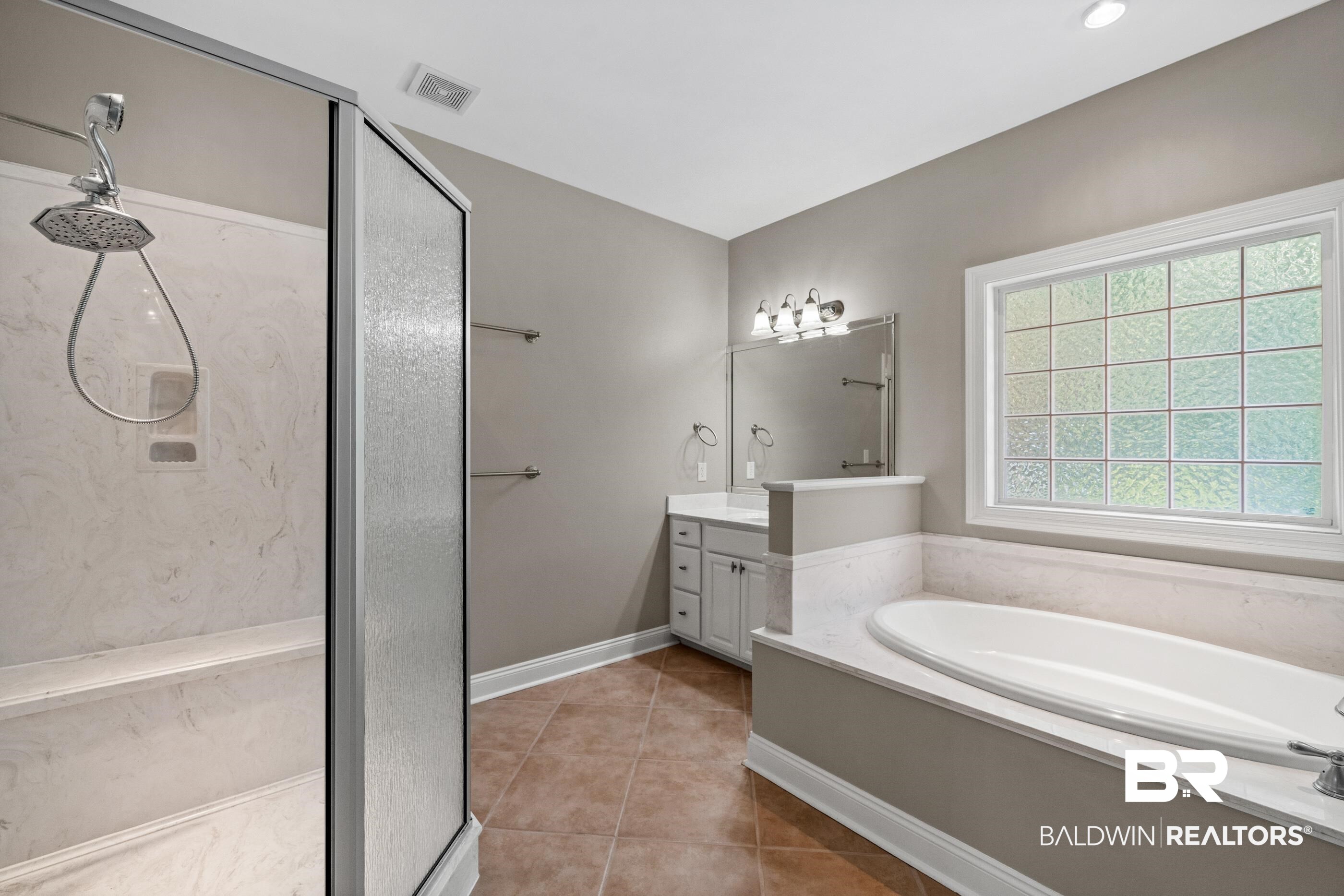 303 Savannah Circle Foley, AL 36535 - Photo 22 of 34 Bathroom featuring a glass-enclosed shower with a built-in bench, a separate soaking tub with a perimeter deck, a single vanity with storage, tile flooring, and a large privacy window