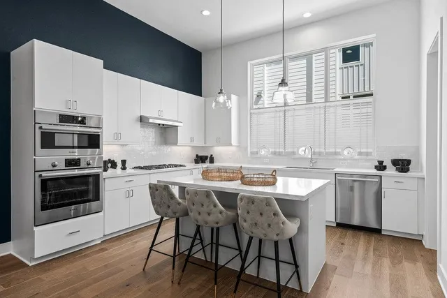 a kitchen with stainless steel appliances granite countertop a stove a sink dishwasher a oven with white cabinets and wooden floor