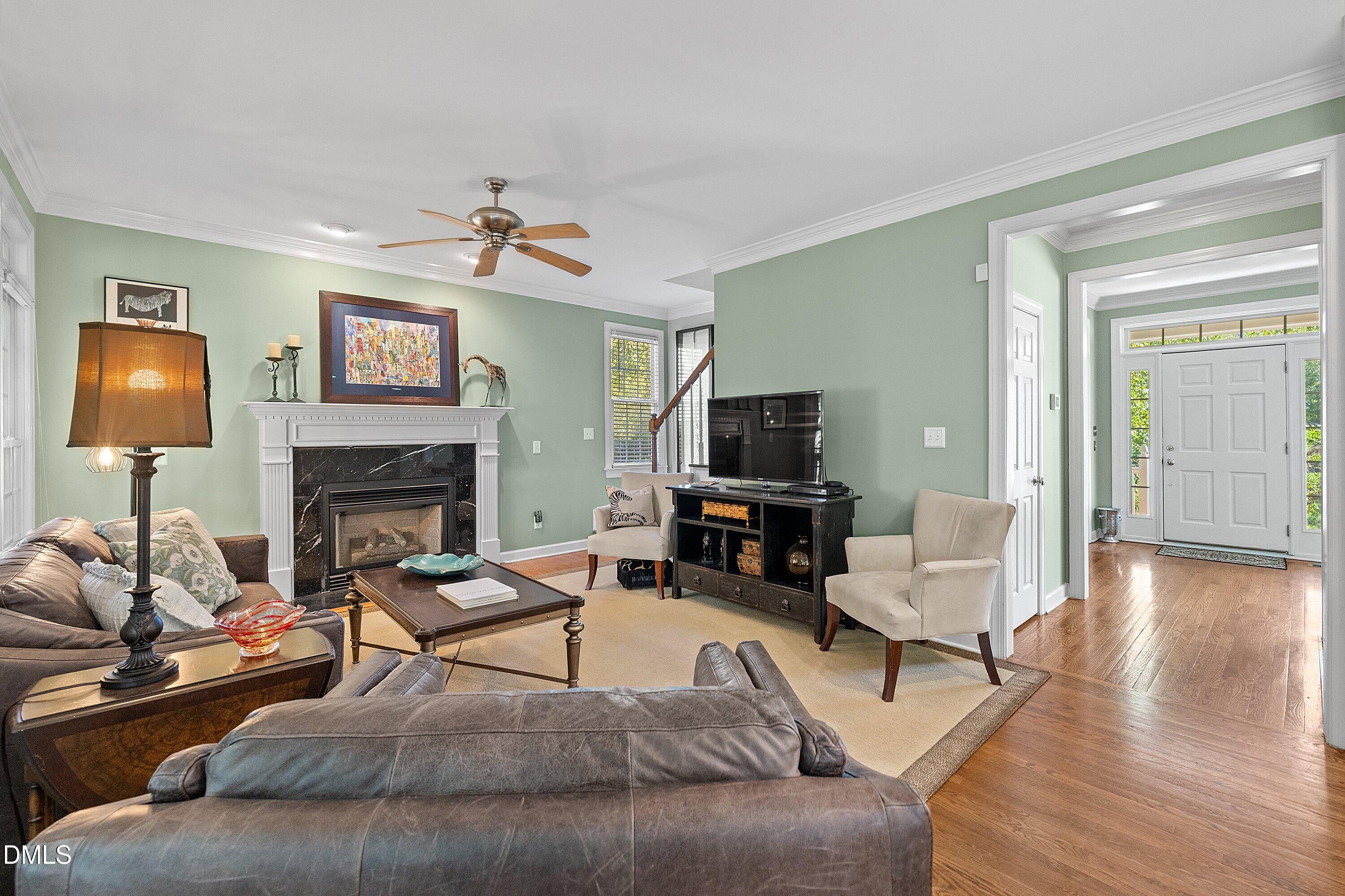 3914 Sterling Ridge Lane Durham, NC 27707 - Photo 16 of 66 Fireplace with a black stone surround and white mantle, ceiling fan with wood-finish blades, hardwood flooring in the entryway, white double entry doors with sidelights and transom window, and a white crown molding throughout
