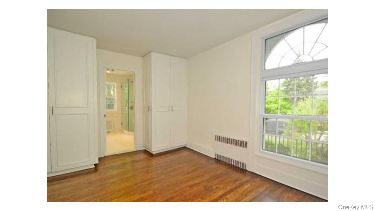 2 Arleigh Road Great Neck, NY 11021 - Photo 13 of 22 Wood-finish flooring with built-in cabinetry, an arched window, and an en-suite bathroom with a glass-enclosed shower