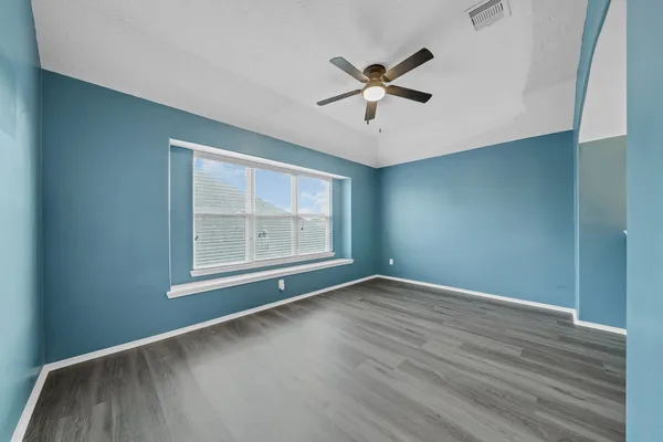 an empty room with wooden floor fan and windows