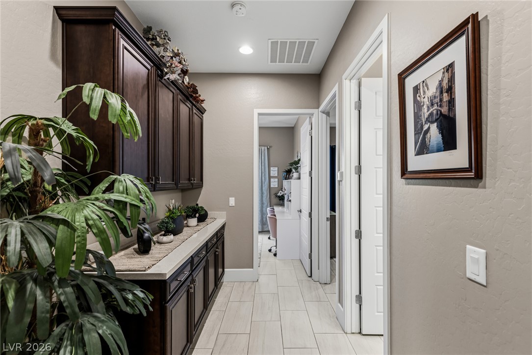 10167 Copper Edge Road Las Vegas, NV 89148 - Photo 20 of 45 A well-appointed hallway with rich cabinetry and durable tile flooring leads to a sun-kissed office space.