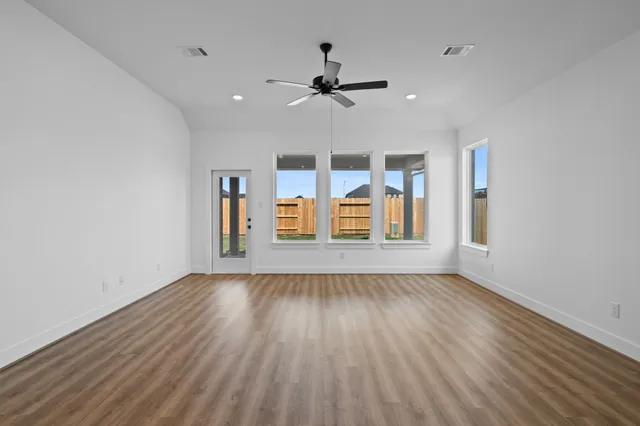 an empty room with wooden floor ceiling fan and windows
