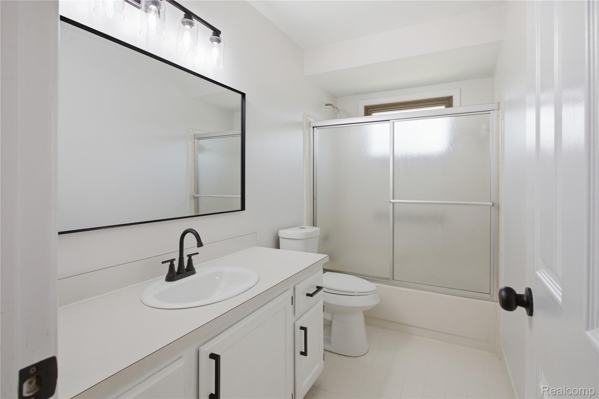 52658 Stag Ridge Drive Macomb, MI 48042 - Photo 25 of 28 Bathroom featuring a vanity with an integrated sink, black hardware, a rectangular mirror, a three-light fixture, and a tub/shower combination with sliding frosted glass doors