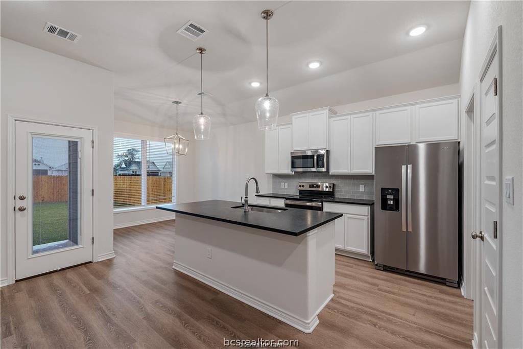 3161 Tarleton Court Bryan, TX 77808 - Photo 8 of 23 a kitchen with stainless steel appliances a refrigerator a sink dishwasher a stove and white cabinets with wooden floor