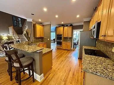 a kitchen with stainless steel appliances granite countertop a stove top oven a sink dishwasher and wooden cabinets with wooden floor
