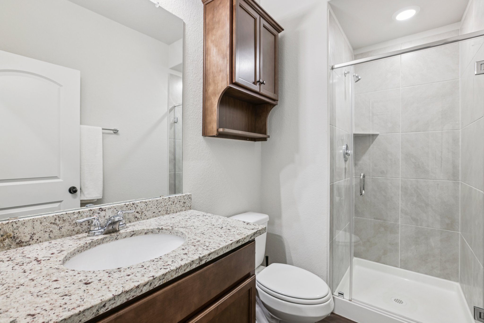 204 Swinging H Lane Georgetown, TX 78633 - Photo 19 of 39 Bathroom with a granite countertop vanity featuring an undermount sink, a glass-enclosed shower with tile surround, and a wooden wall-mounted cabinet