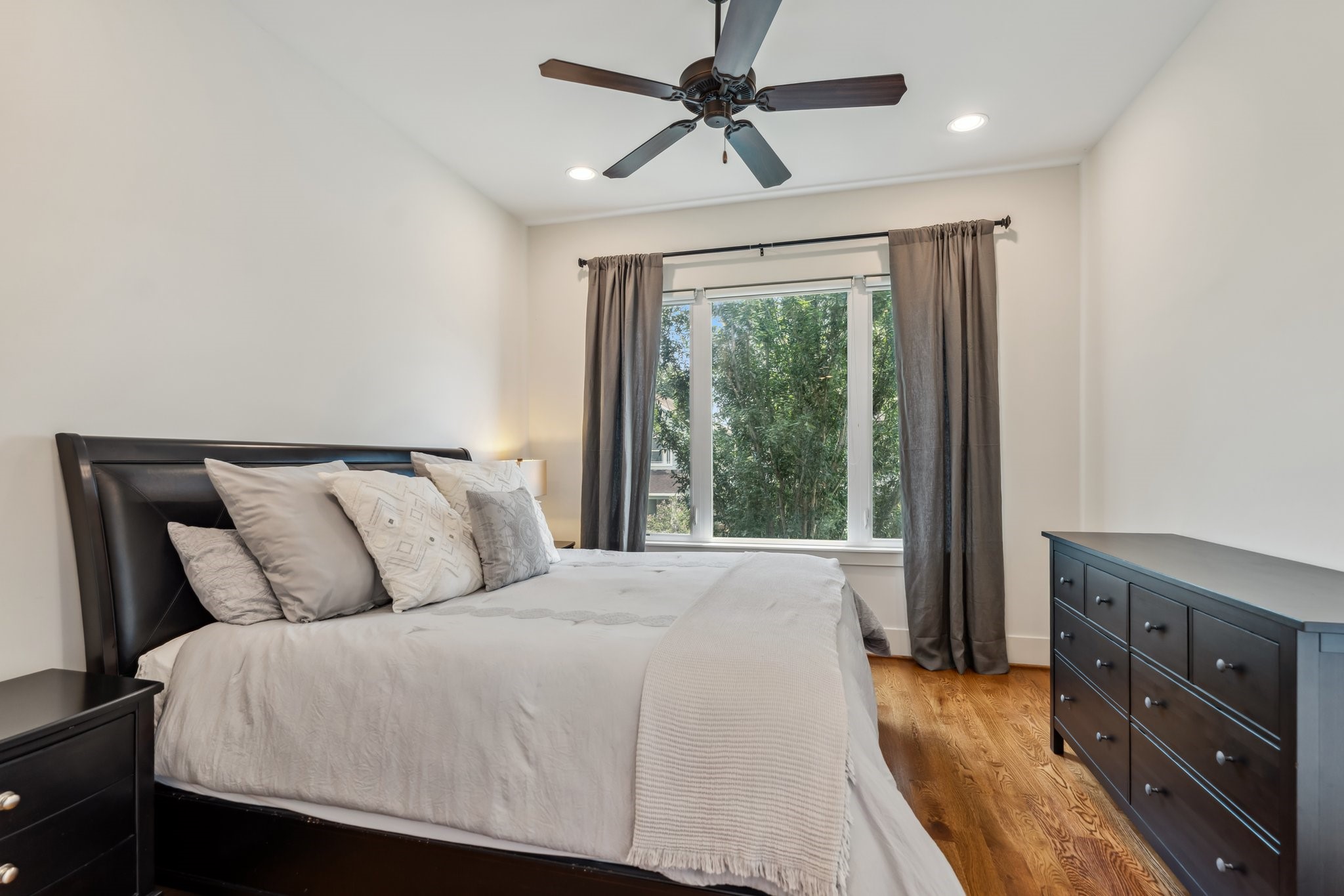 815 East 27th Street Houston, TX 77009 - Photo 24 of 44 Located upstairs with peaceful views overlooking the front yard, this charming secondary bedroom #2 offers hardwood floors, recessed can lighting, and a ceiling fan for comfort. Large windows provide a serene view of the trees, and pull-down blackout shades paired with drapes allow for privacy and light control. This spacious room is perfect for a guest, child, or home office. It also has a private ensuite bathroom.