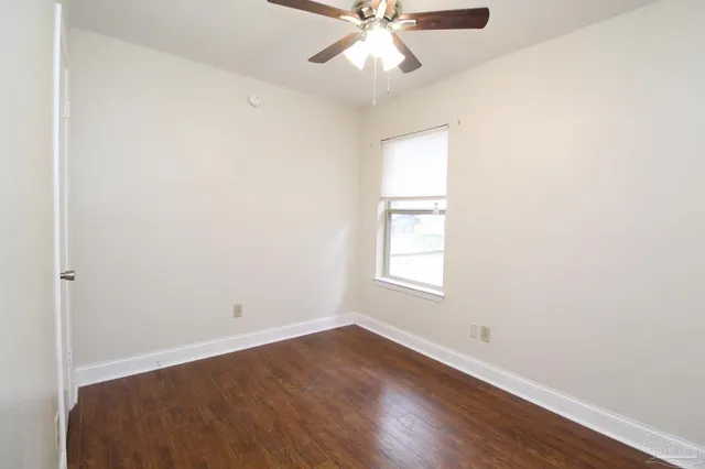an empty room with wooden floor fan and windows