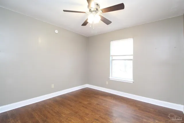 an empty room with wooden floor fan and windows