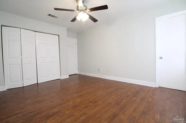 an empty room with wooden floor fan and windows
