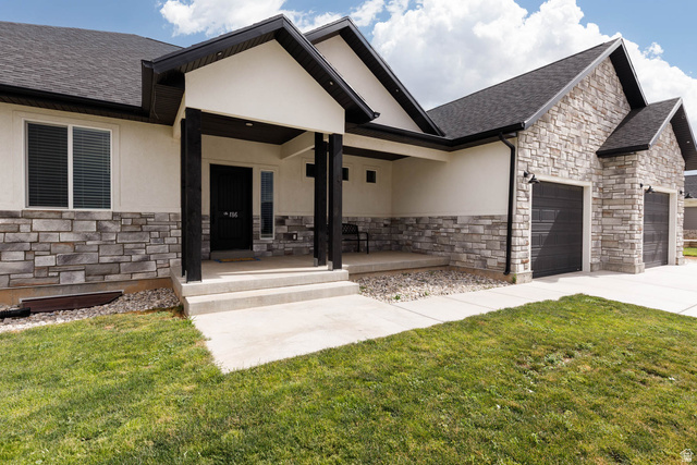 186 West 580 North Redmond, UT 84652 - Photo 2 of 74 View of front of house with stone siding, a porch, stucco siding, an attached garage, and a front lawn