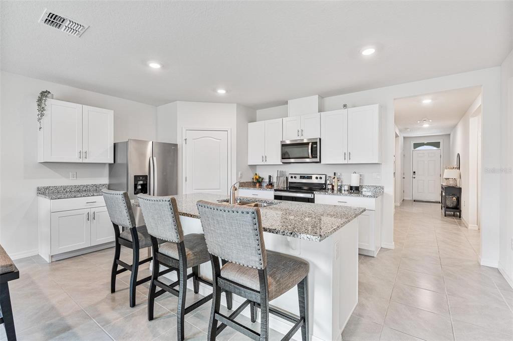 511 Baroness Way DeLand, FL 32724 - Photo 9 of 37 a kitchen with stainless steel appliances kitchen island granite countertop a table chairs microwave and refrigerator