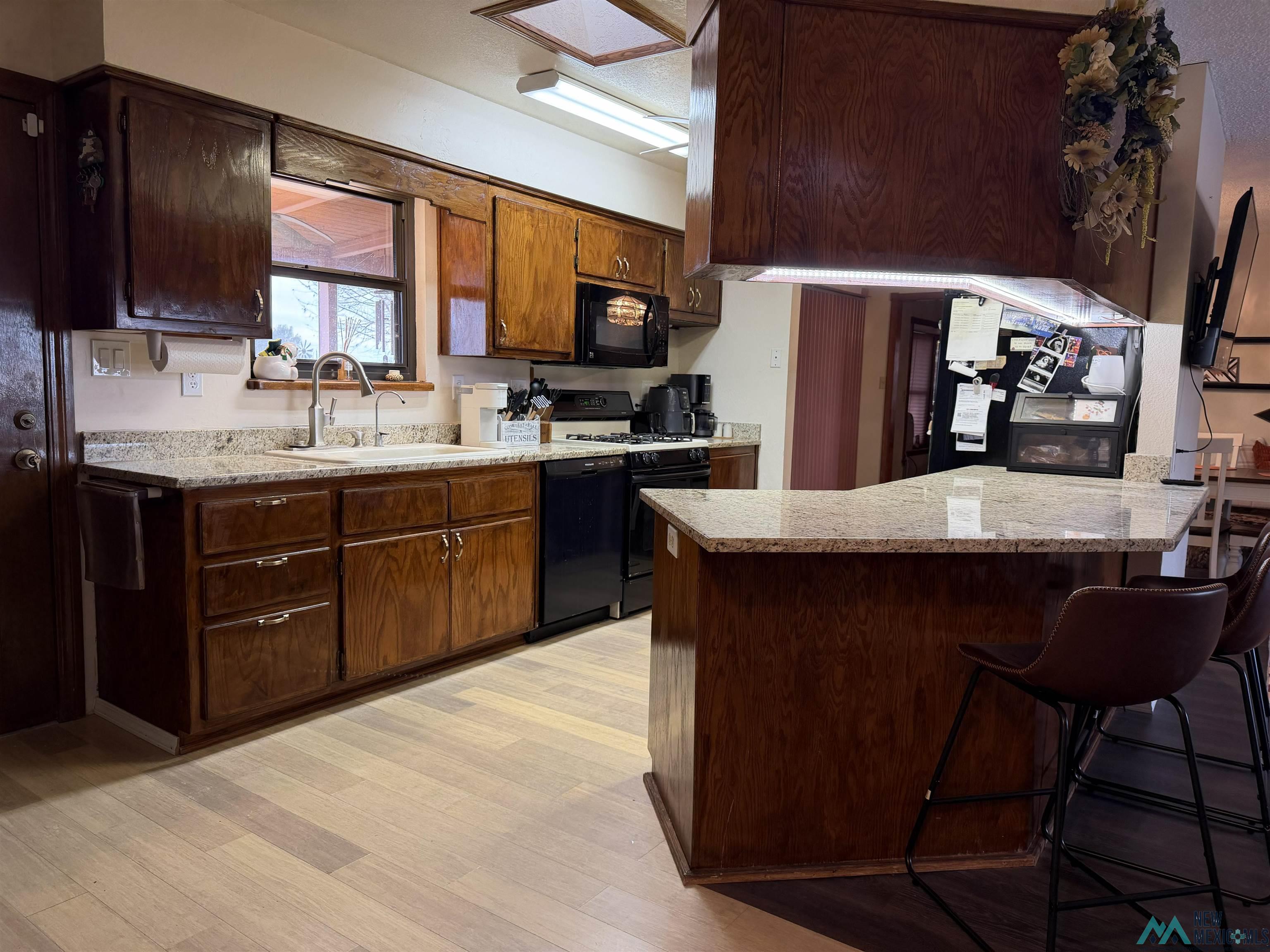2001 East Derrick Road Carlsbad, NM 88220 - Photo 50 of 84 Kitchen featuring black appliances, a breakfast bar, a peninsula, light wood finished floors, and light stone counters