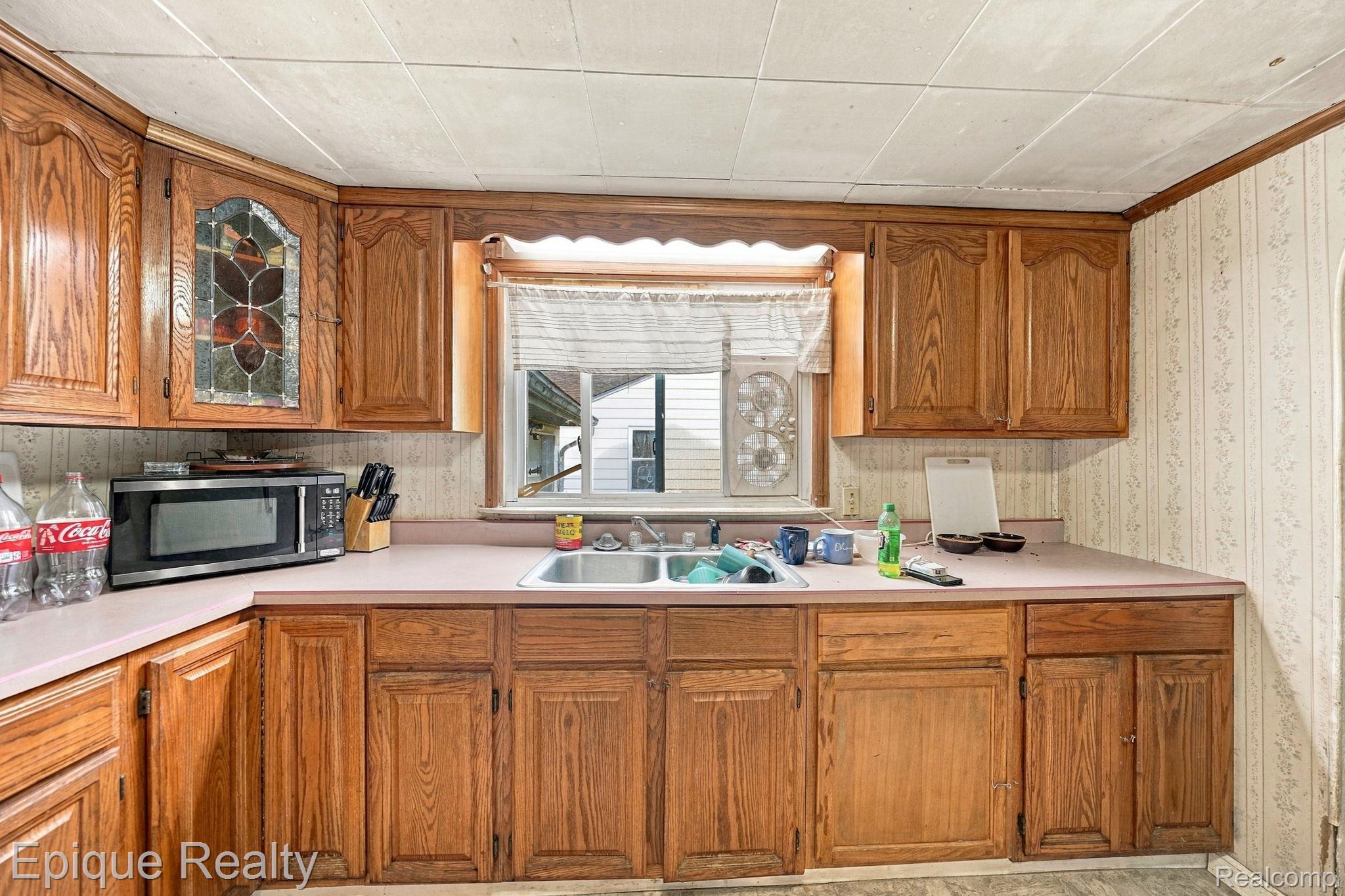4033 Risedorph Street Burton, MI 48509 - Photo 11 of 25 Wood cabinetry with a decorative glass-front corner cabinet, dual basin stainless steel sink, and light-toned countertops