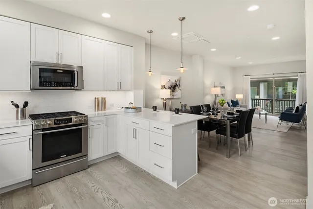 a open kitchen with stainless steel appliances kitchen island granite countertop a stove top oven a sink dishwasher a dining table and chairs with wooden floor