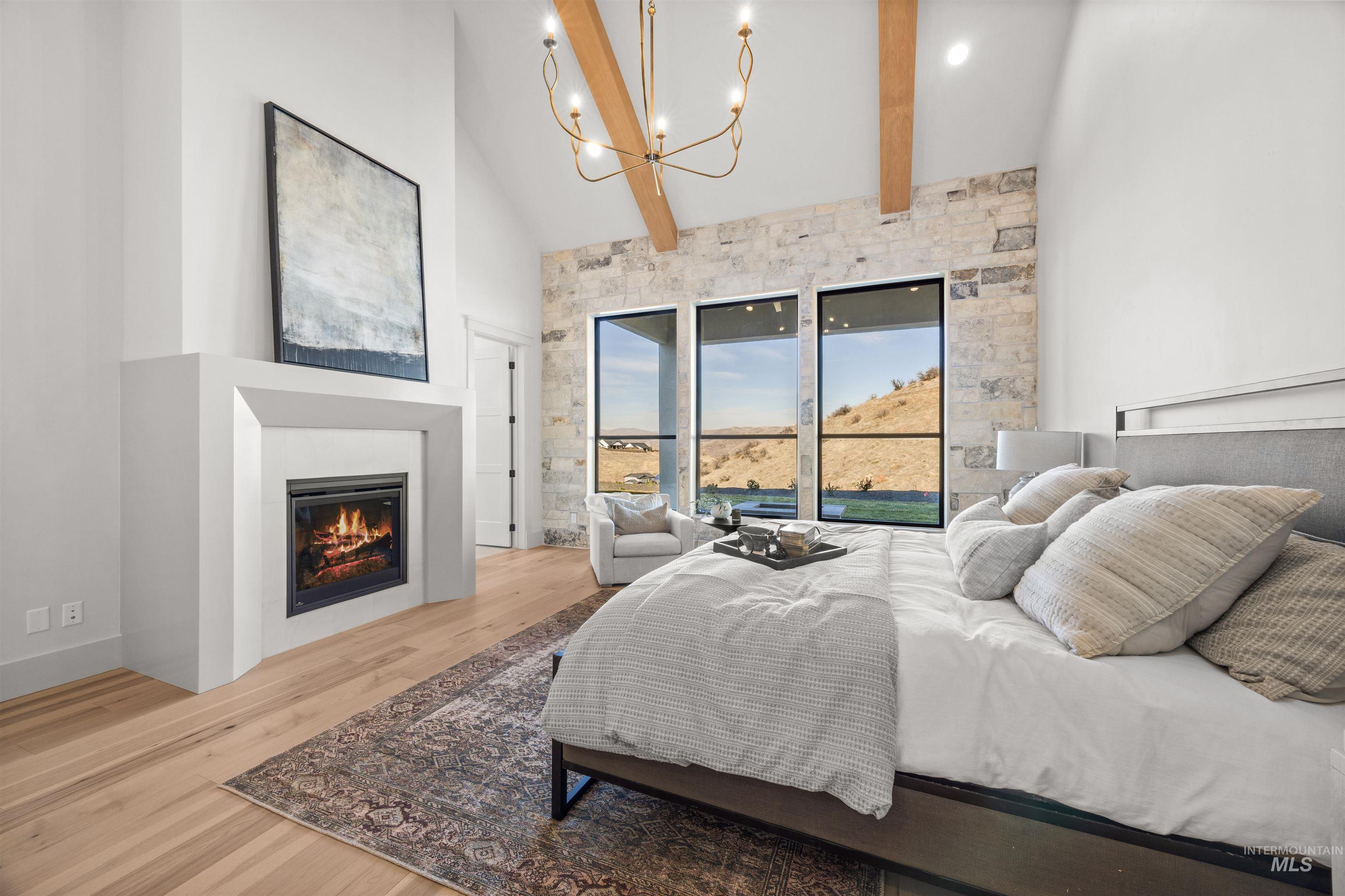 10968 North Elk Ridge Place Boise, ID 83714 - Photo 21 of 49 Bedroom with light wood finished floors, a glass covered fireplace, lofted ceiling, and a chandelier