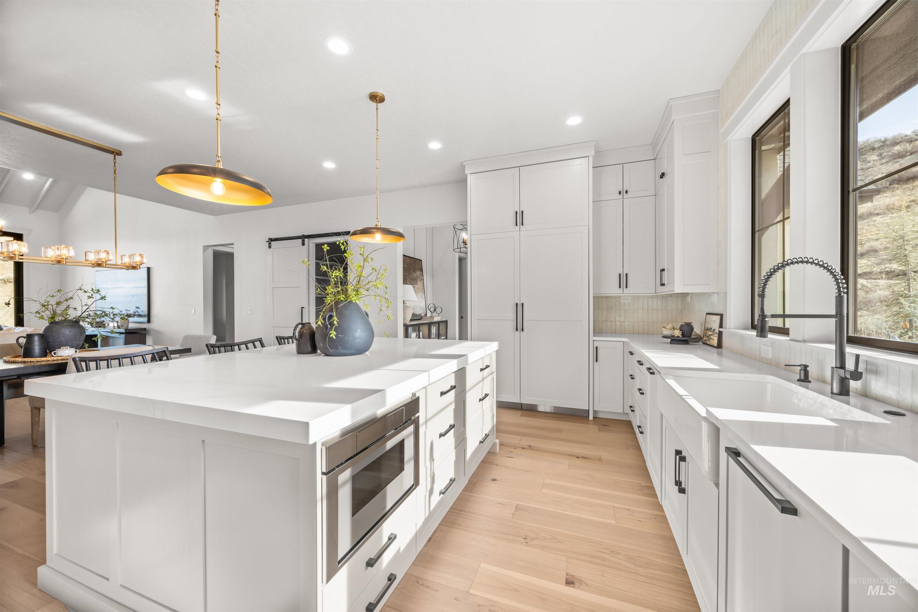 10968 North Elk Ridge Place Boise, ID 83714 - Photo 9 of 49 Kitchen with white cabinets, light wood-style floors, a barn door, hanging light fixtures, and a kitchen island