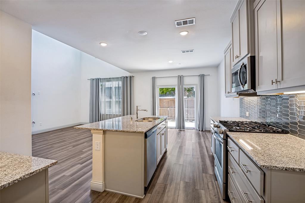 1006 Emil Place Allen, TX 75013 - Photo 10 of 28 Kitchen with wood-finish flooring featuring granite countertops, stainless steel appliances, a tile backsplash, and an island with a built-in sink