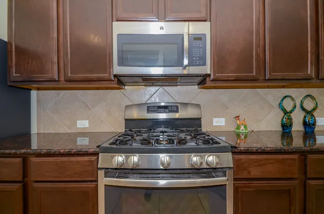 a kitchen with stainless steel appliances granite countertop a stove top oven a sink dishwasher a dining table and chairs with wooden floor