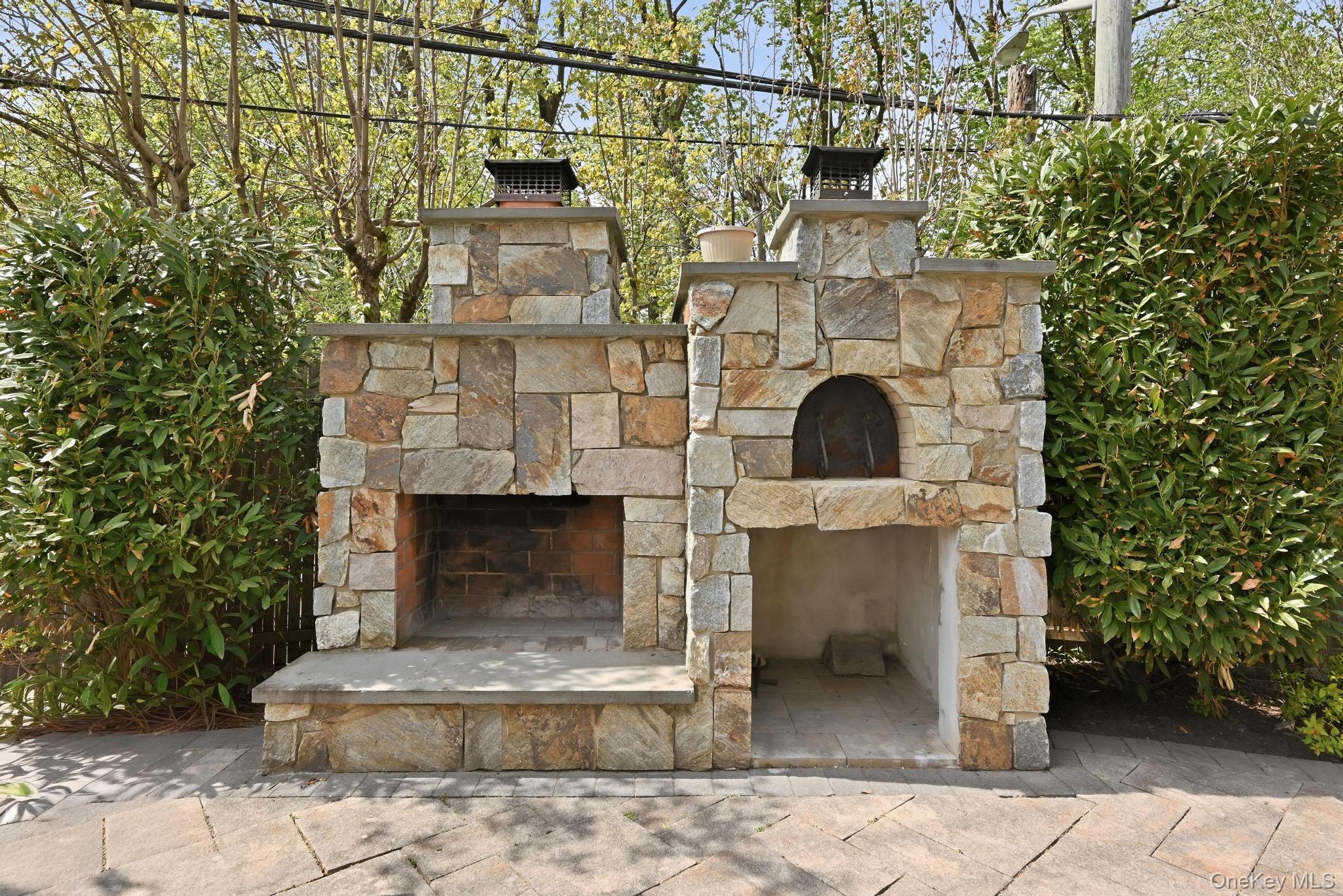 42 Skunks Misery Road Locust Valley, NY 11560 - Photo 43 of 50 Outdoor stone fireplace and pizza oven combination with chimney caps, set on a stone paver patio