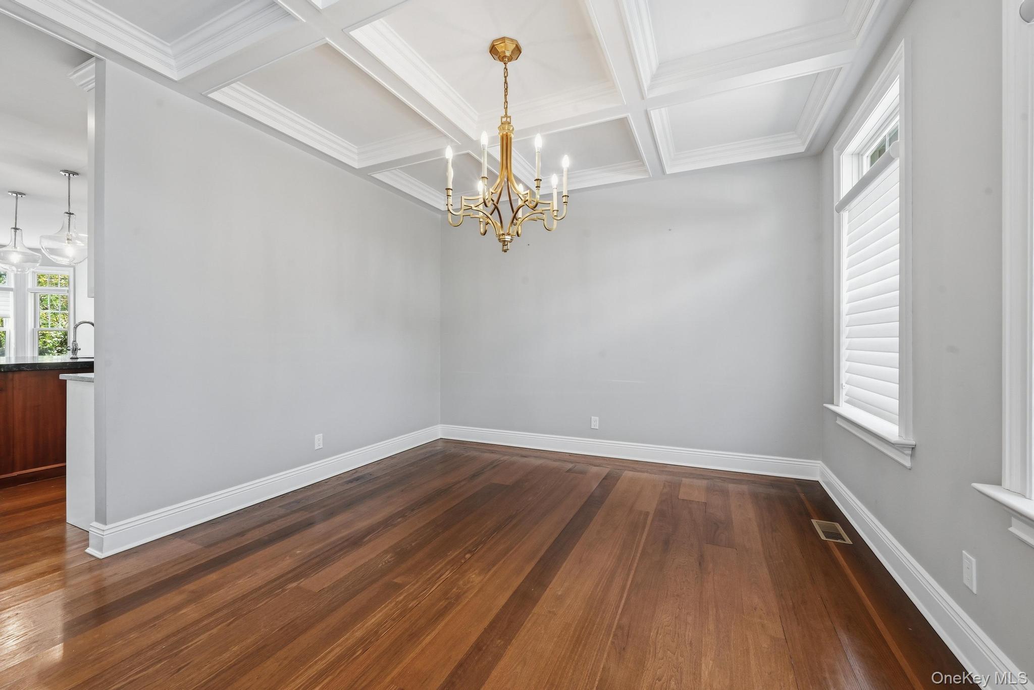 42 Skunks Misery Road Locust Valley, NY 11560 - Photo 5 of 50 Formal dining space featuring coffered ceilings, a gold-toned chandelier, wood-finish flooring, white baseboards, and window treatments