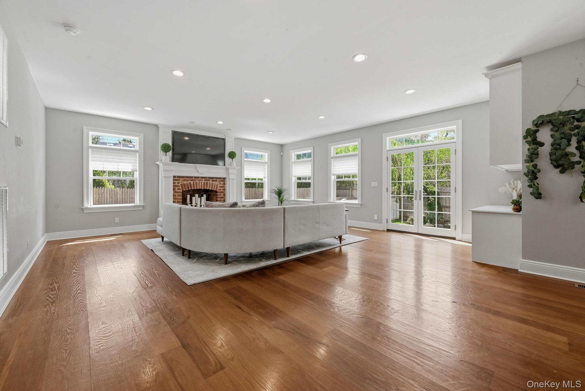 42 Skunks Misery Road Locust Valley, NY 11560 - Photo 7 of 50 Spacious living area featuring rich wood-finish flooring, a brick fireplace with a white mantel, recessed lighting, and multiple windows for abundant natural light