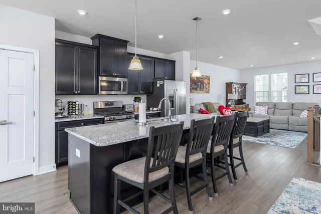 a kitchen with stainless steel appliances kitchen island granite countertop a dining table chairs refrigerator and microwave