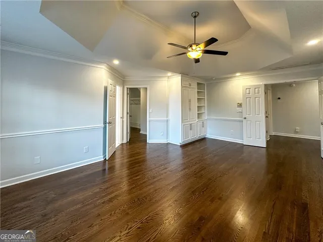 a view of an empty room with wooden floor and a ceiling fan