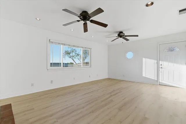 an empty room with wooden floor fan and windows